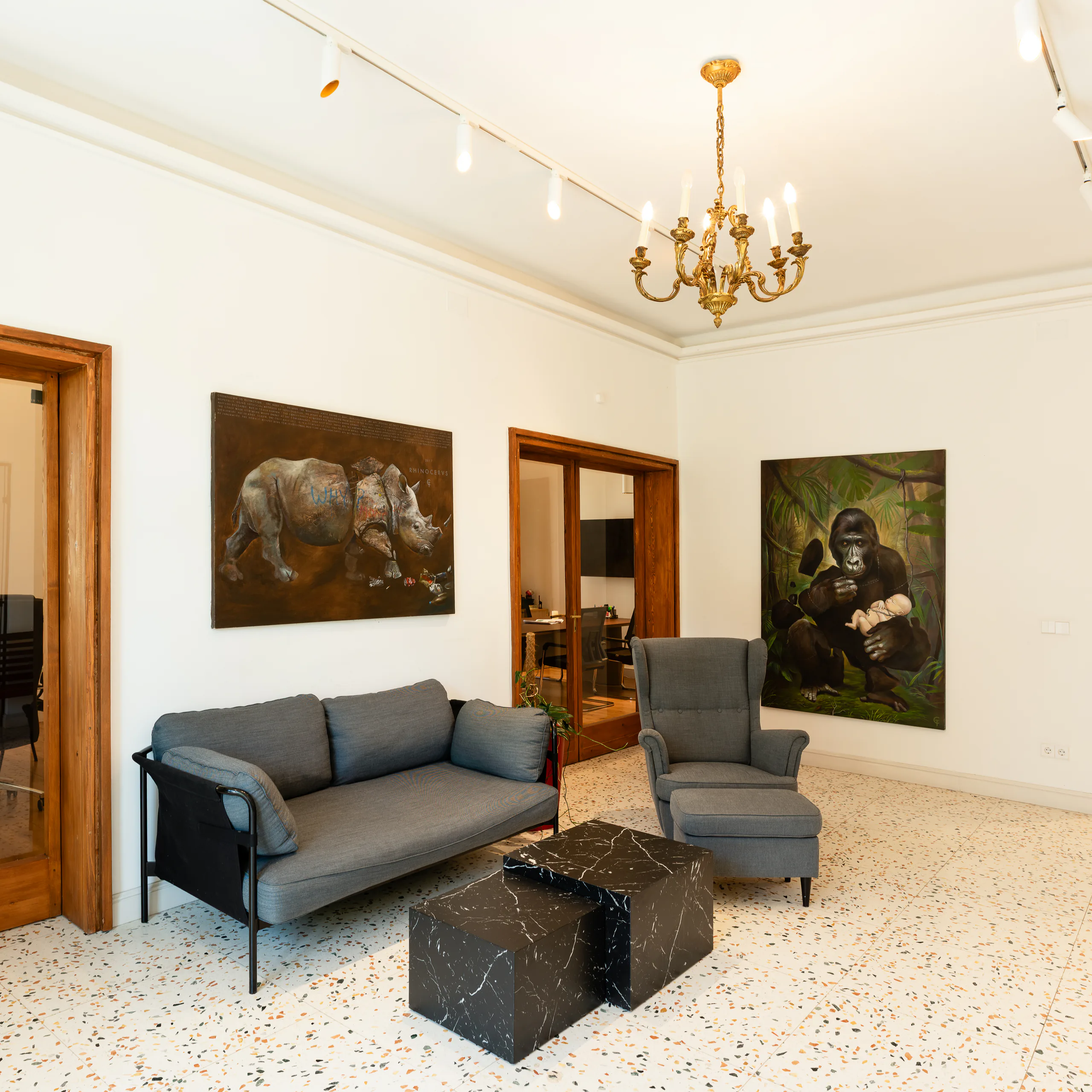 Lobby with a terrazzo floor, gilded chandelier, grey sofa, marble side tables and rhino and gorilla paintings