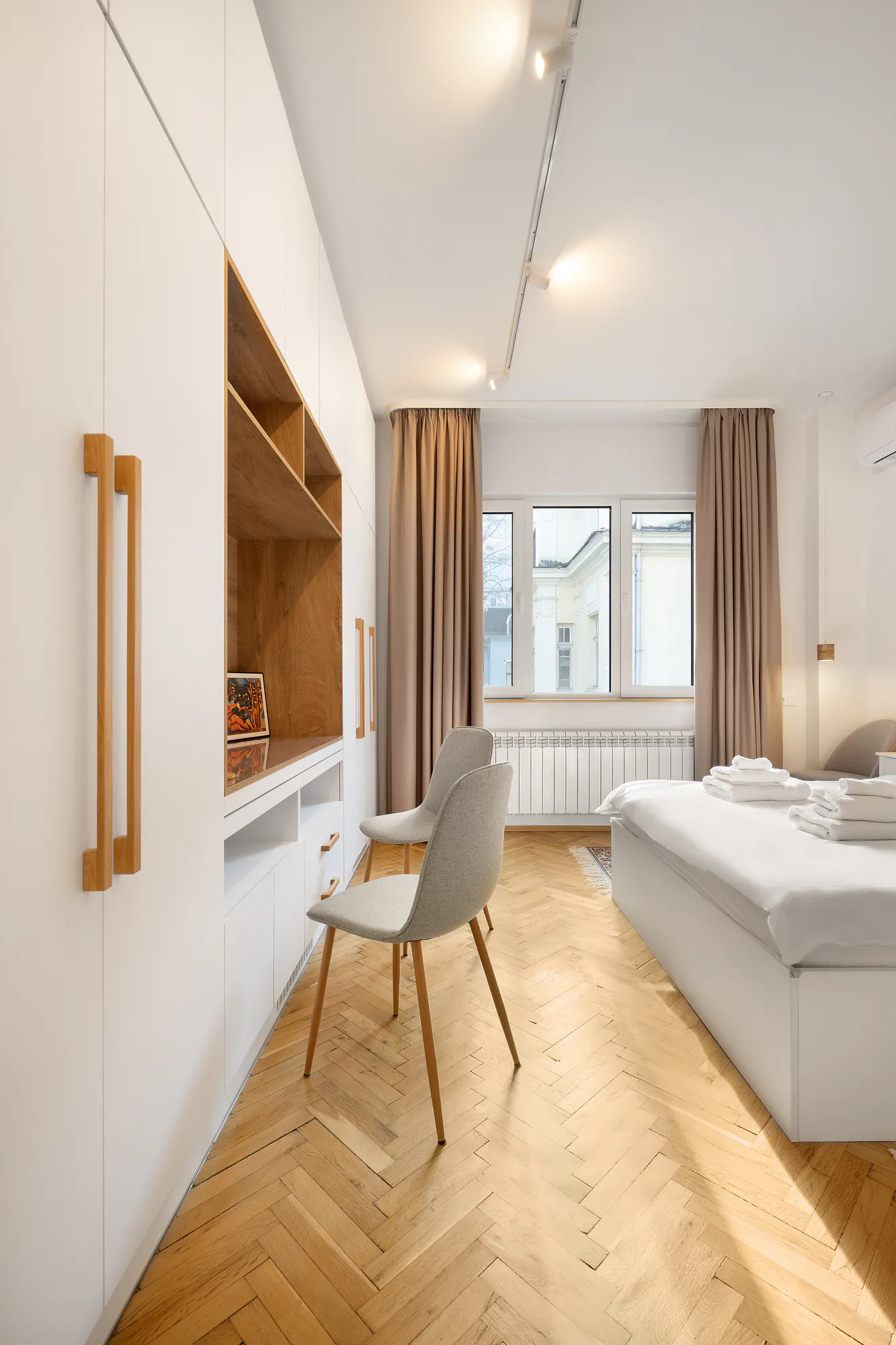 Bedroom with a workspace, built-in white wardrobe with wooden handles and track lighting