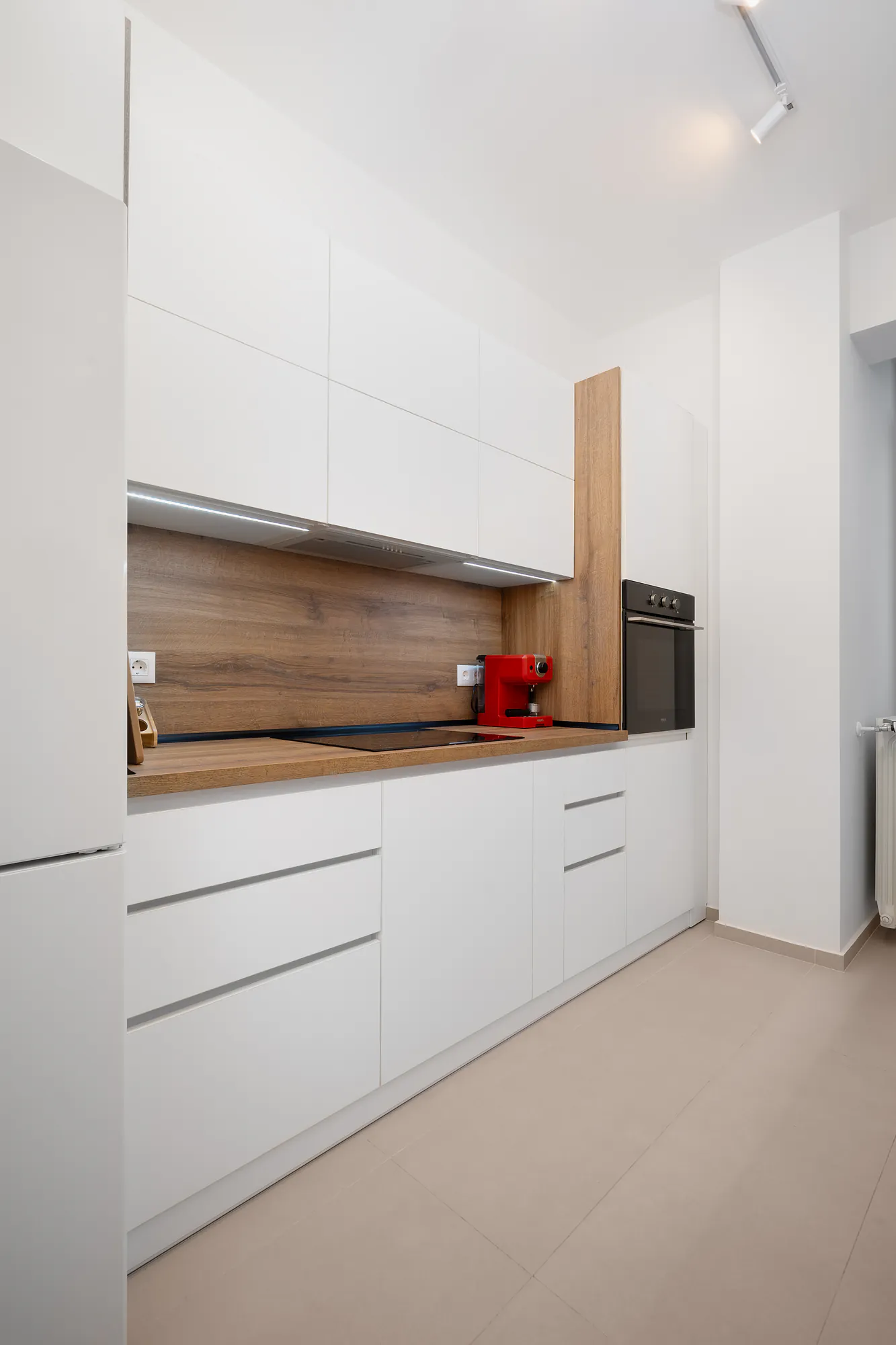 Handleless white kitchen with a wooden splashback, wooden worktop and built-in oven