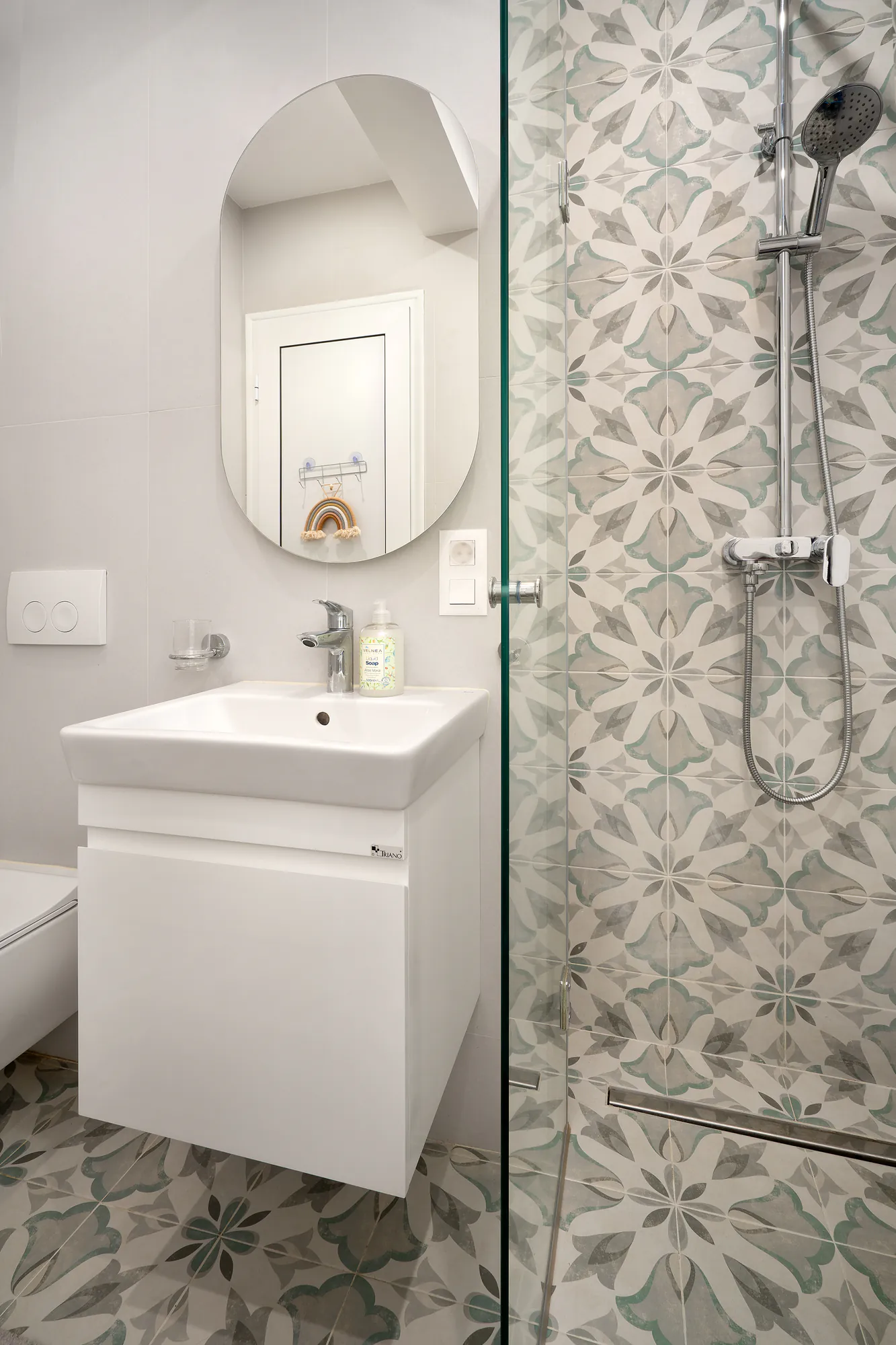 Bathroom with a shower enclosure, oval mirror and floral-pattern tiles on the floor and wall