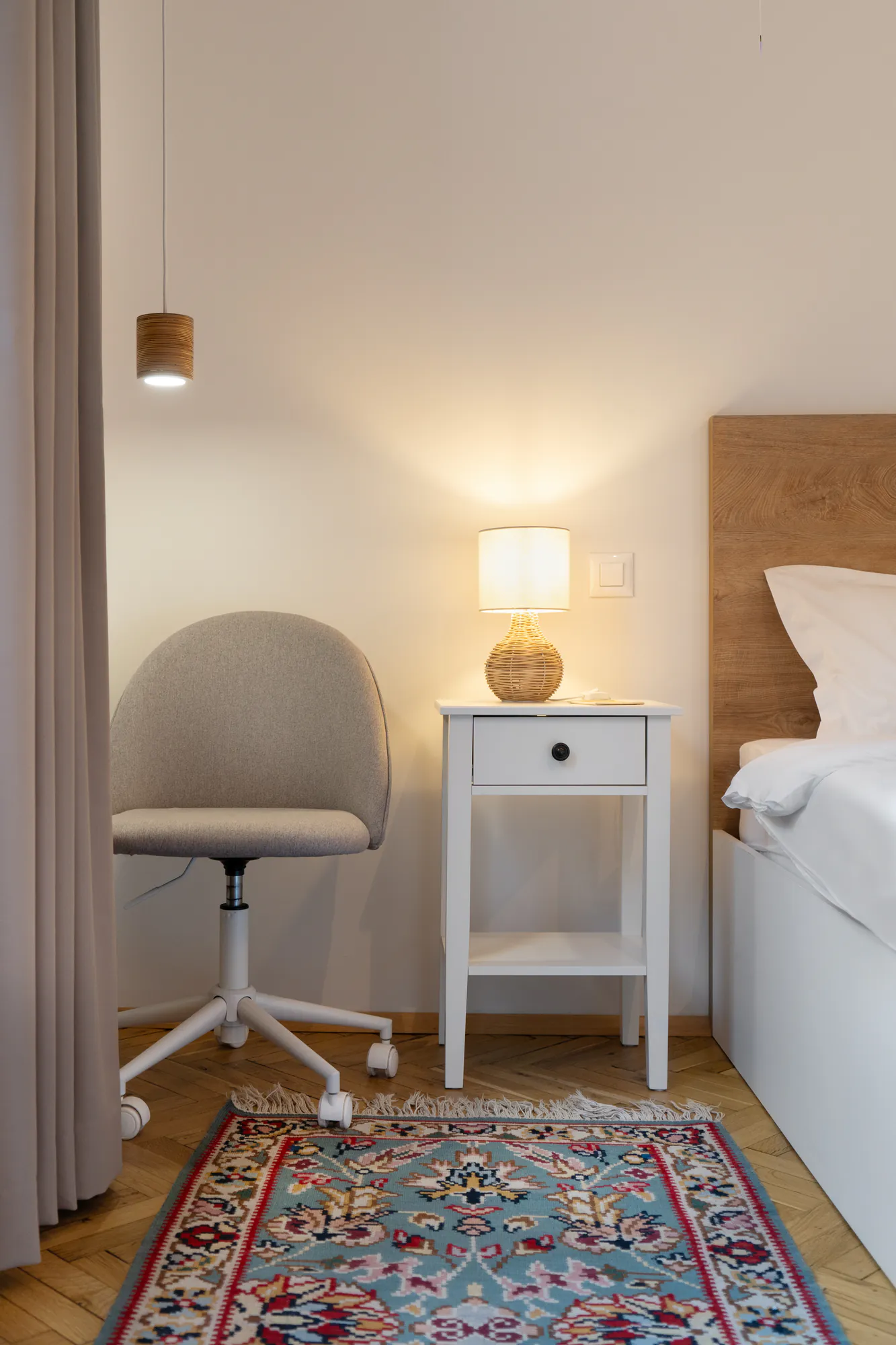 Bedroom detail: white bedside table with a rattan lamp, chair and patterned rug