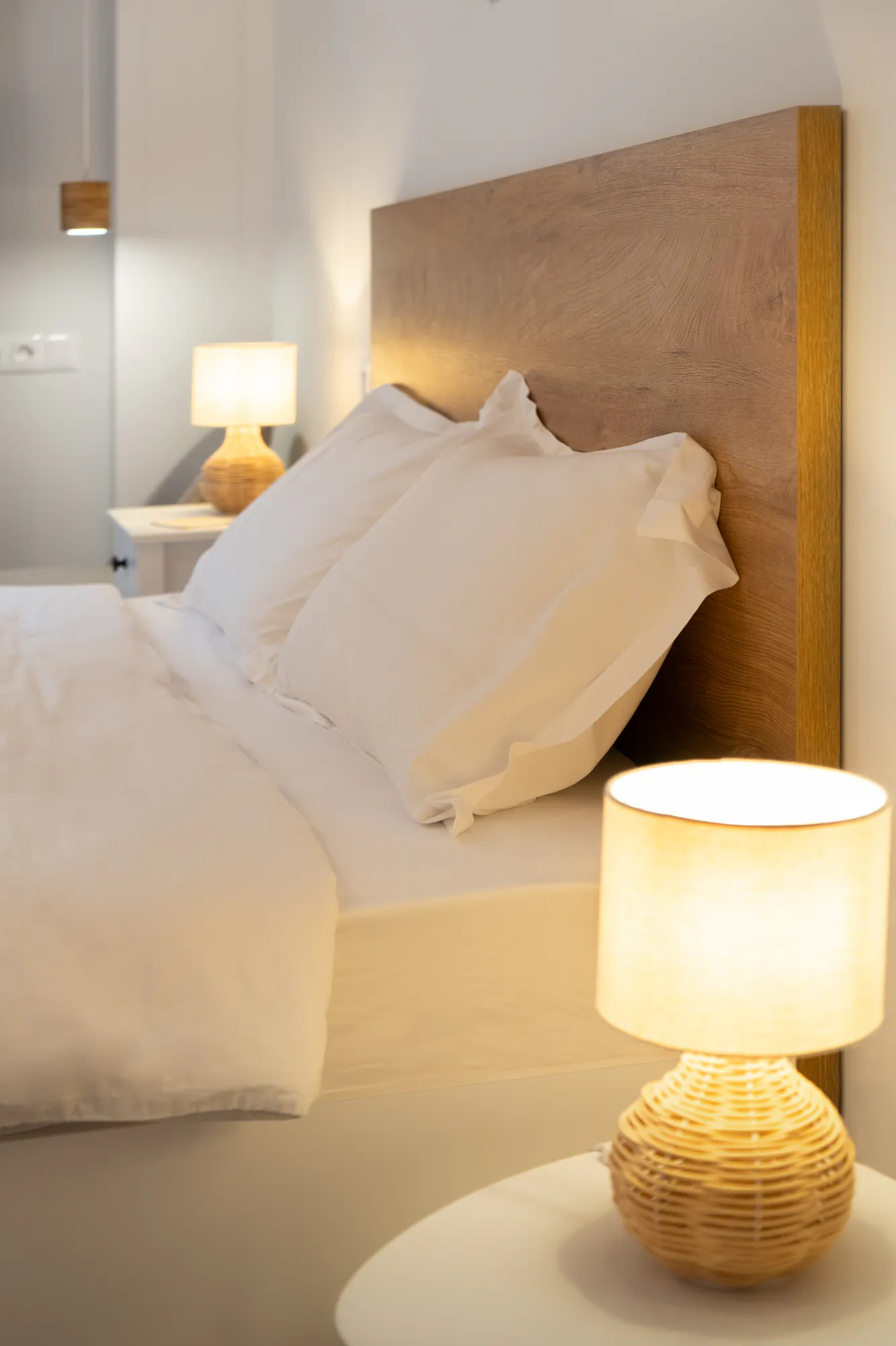 Bedroom detail: wooden headboard, white pillows and warm light from a rattan lamp