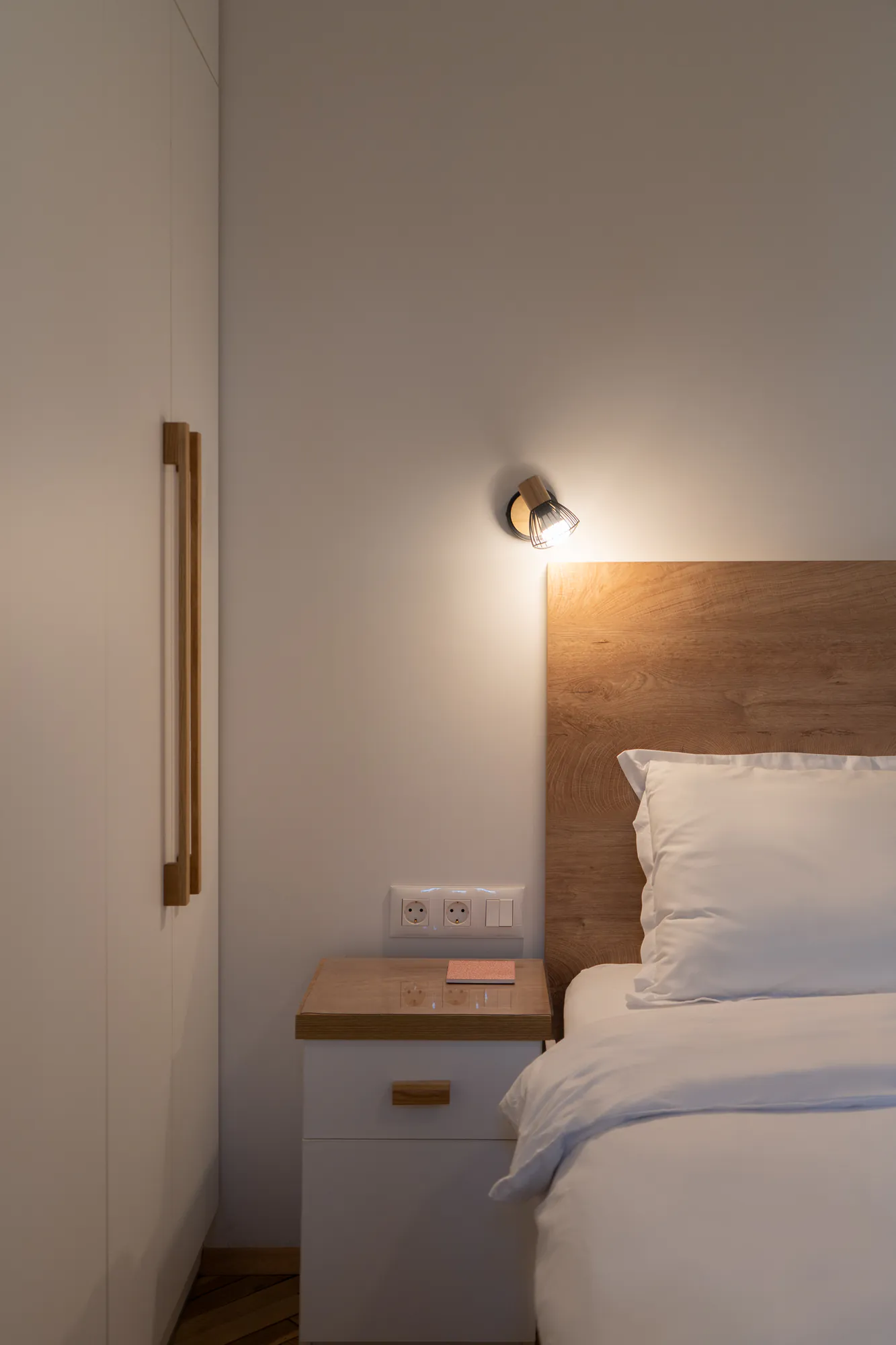 Bedroom detail: wall light above the wooden headboard and a bedside table with a wooden handle