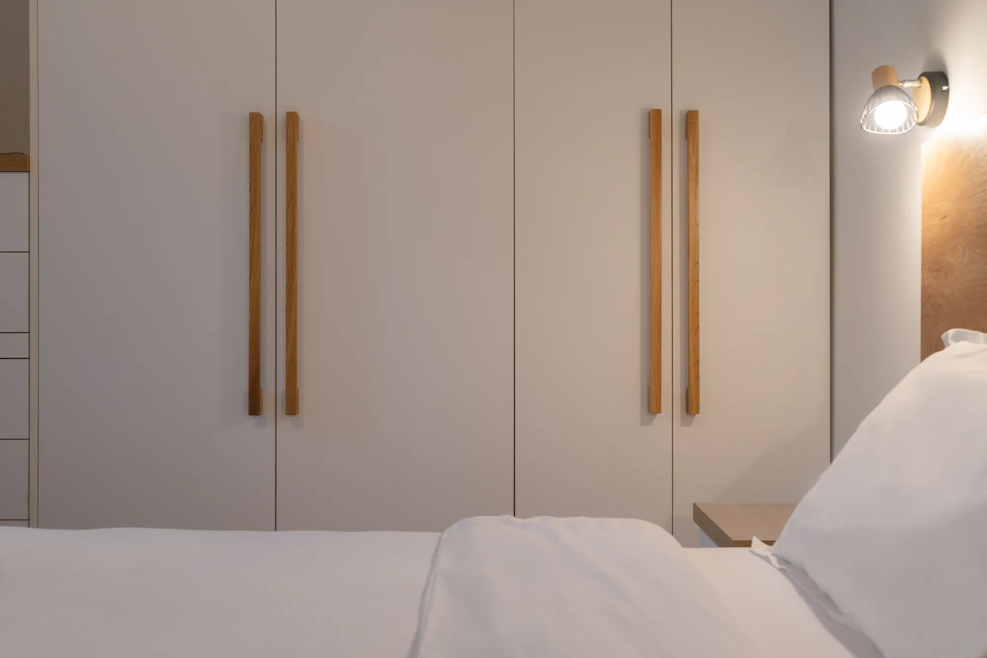 Detail: white wardrobe with long wooden handles next to the bed