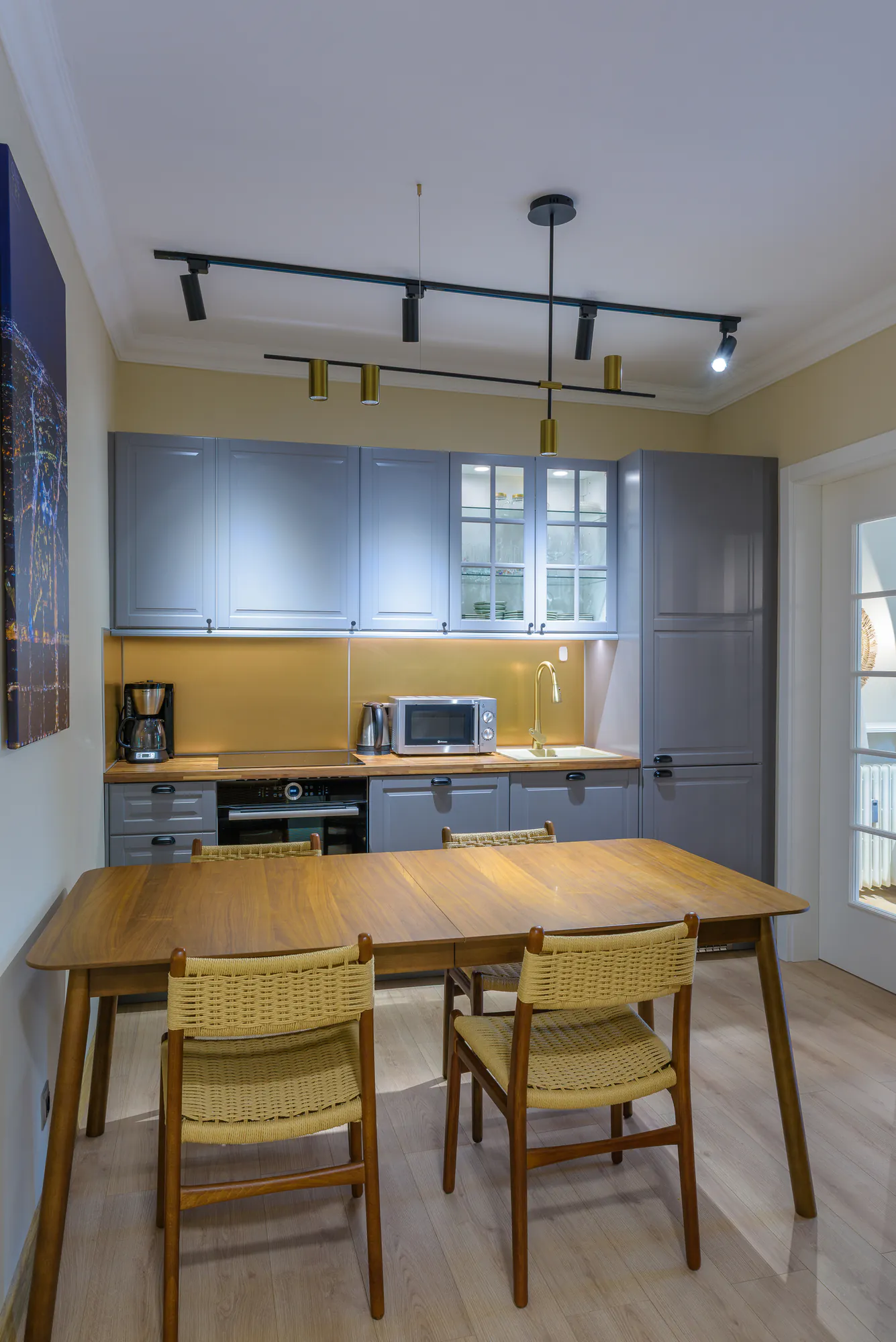 Dining table with woven chairs in front of the grey kitchen and brass lights