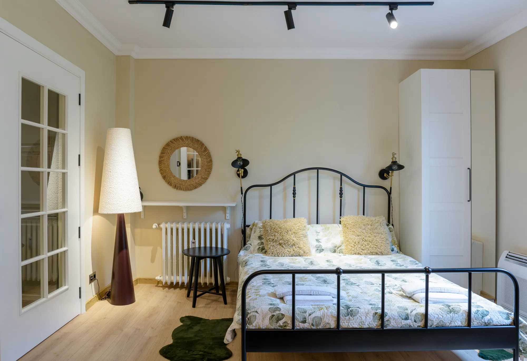 Bedroom with a black metal bed, rattan mirror and a tall floor lamp
