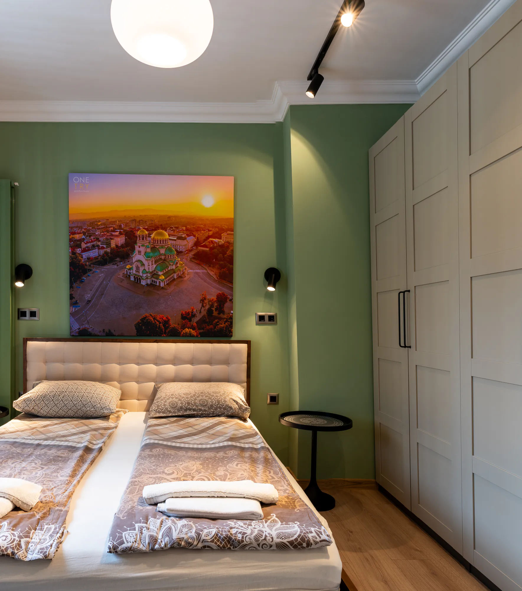 Green bedroom with a white wardrobe, a painting and wall lights