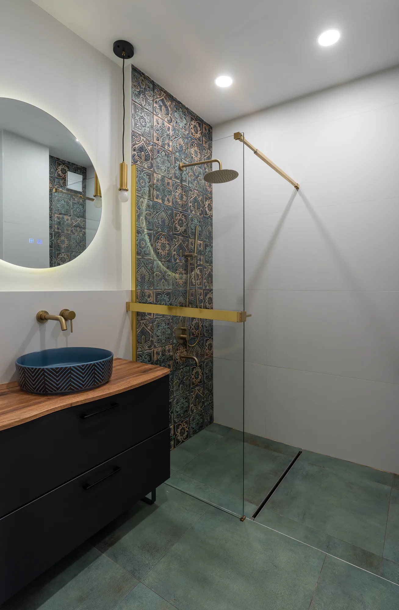 Bathroom with decorative blue tiles, a brass shower and a backlit round mirror