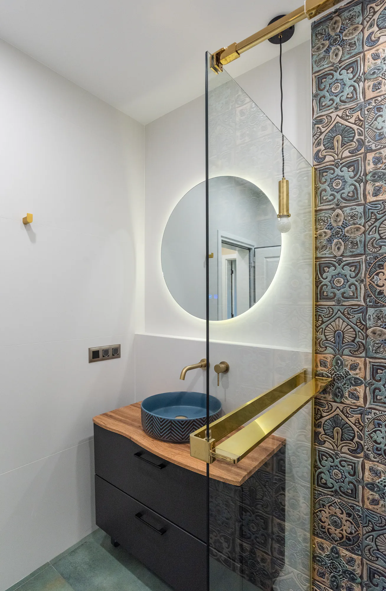 Bathroom with a ceramic basin on a wooden top, black cabinet and brass shower frame