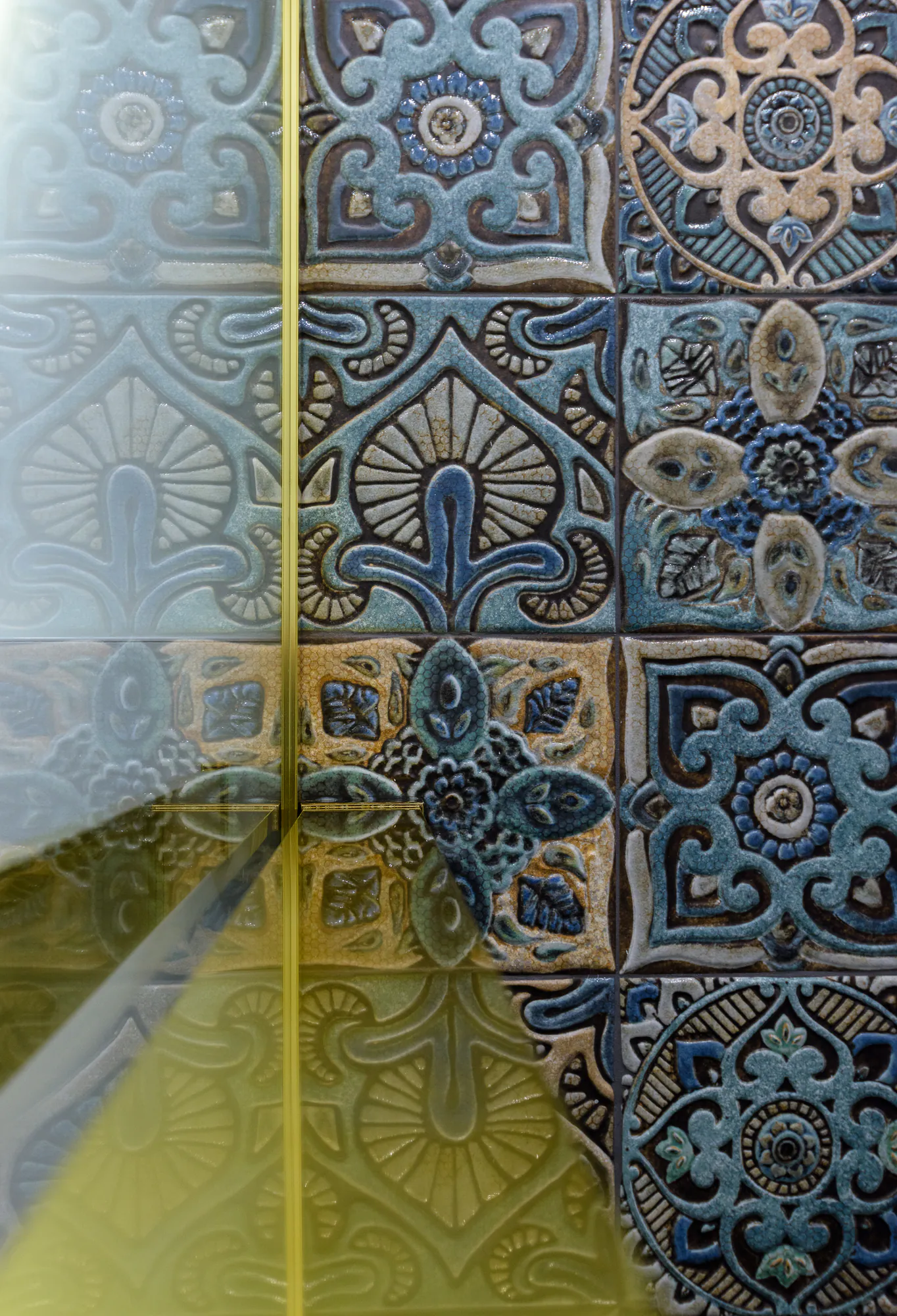 Decorative tiles seen through the glass and brass shower frame