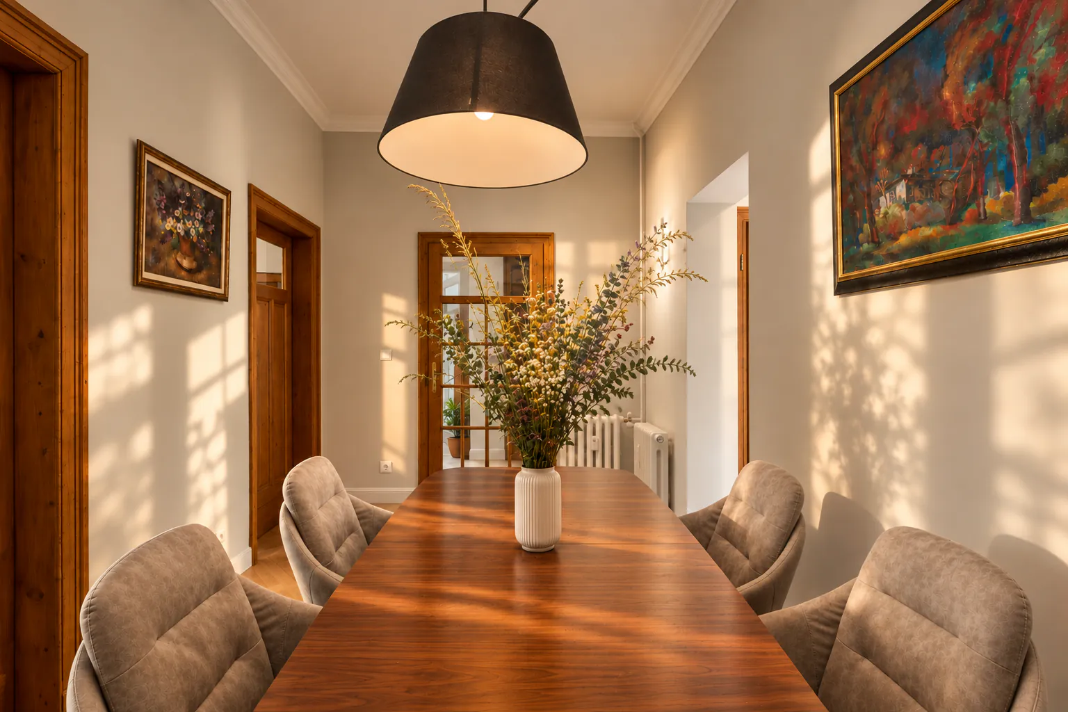 Dining table with a black pendant, a bouquet and paintings in warm afternoon light