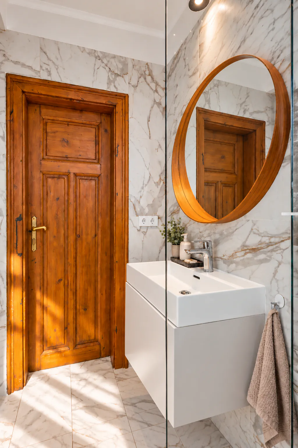 Bathroom with an original wooden door, a wall-hung white basin and a round mirror